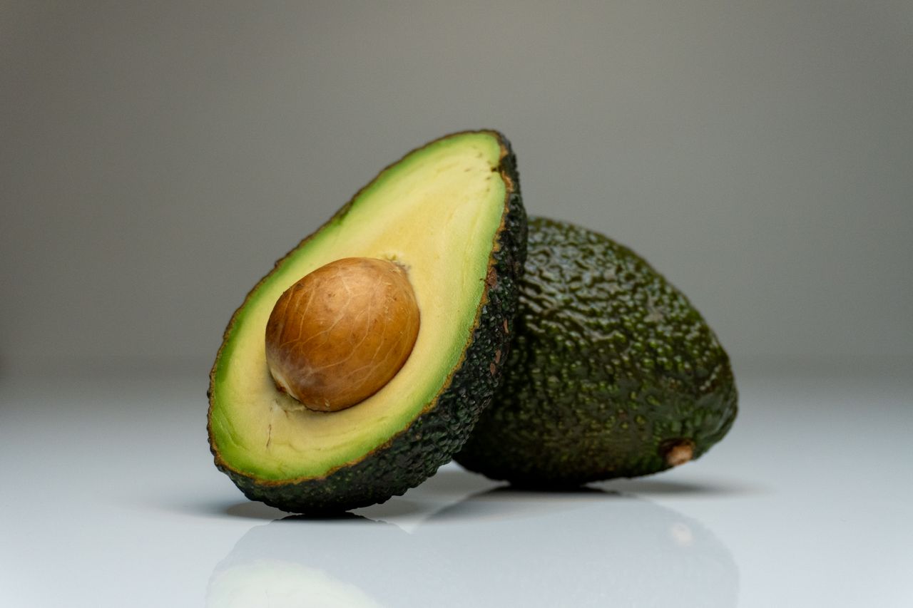 about-01 Close-up of a halved avocado with seed, showcasing vibrant colors on a reflective white background.
