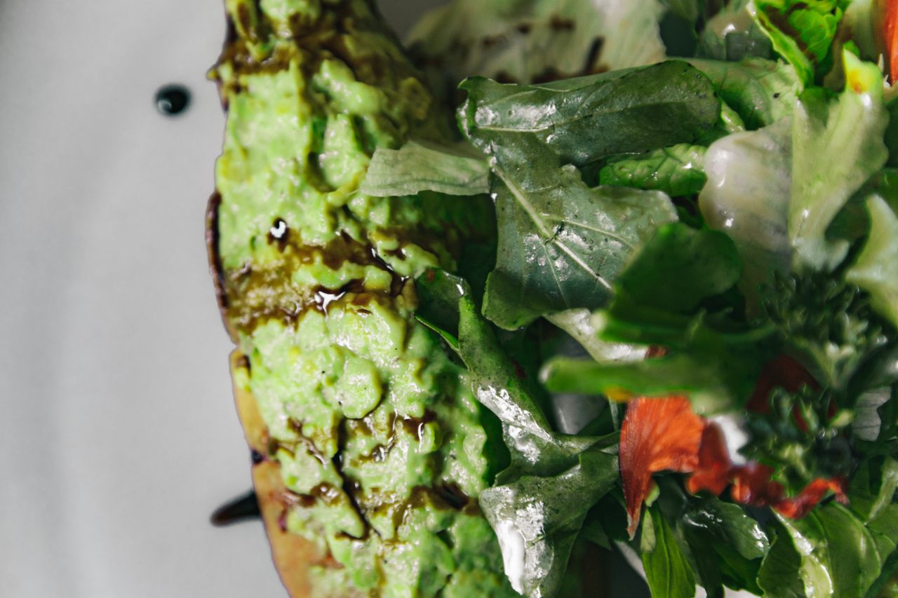Close-up of avocado toast topped with fresh mixed greens and balsamic drizzle.