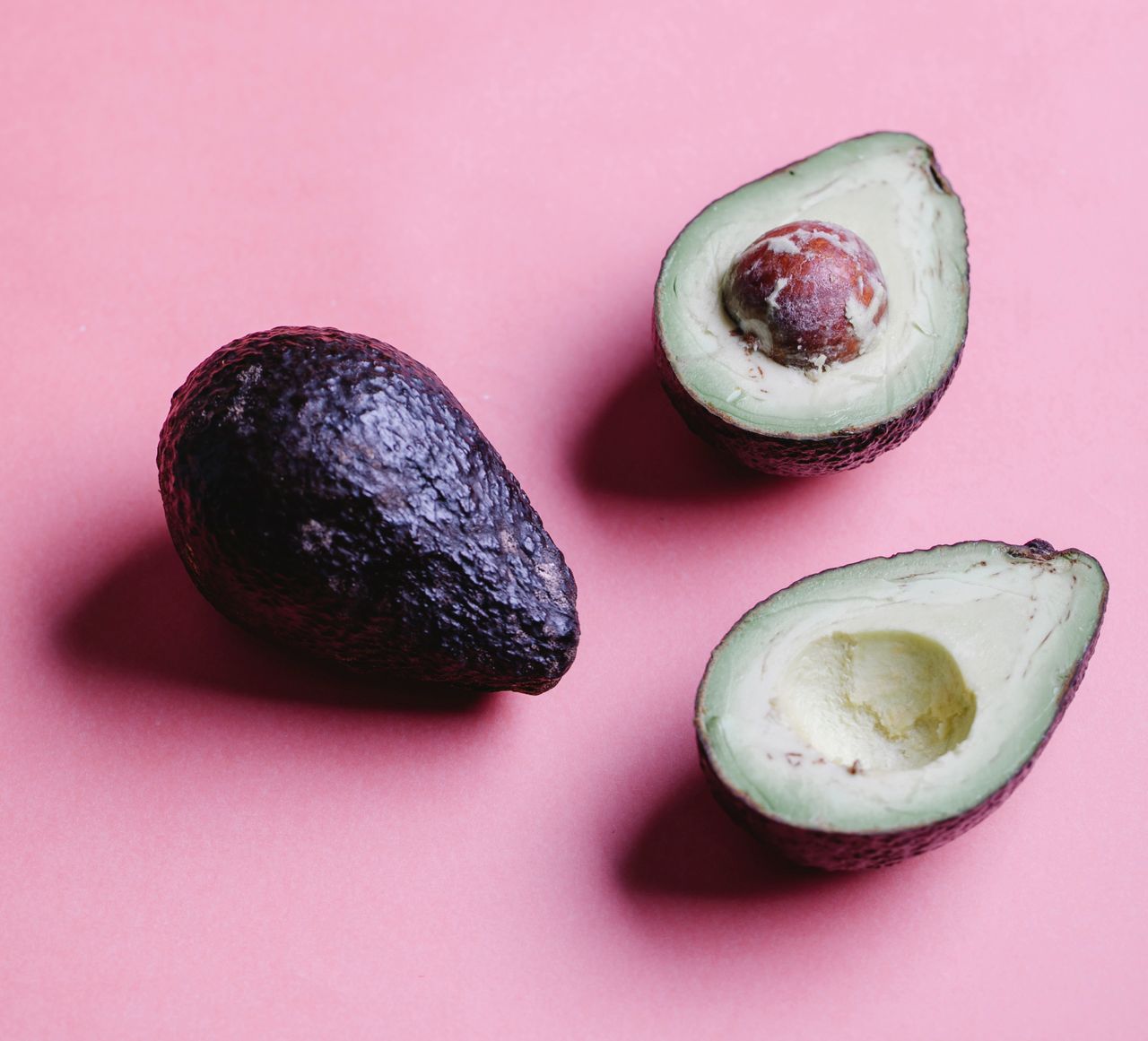 gallery-1 Arrangement of ripe whole and halves of avocados with round seed and flash placed on pink background in bright studio