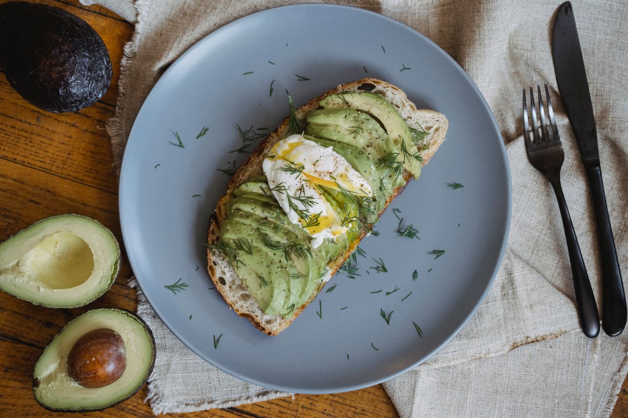 Healthy avocado toast topped with poached egg and dill on a gray plate.
