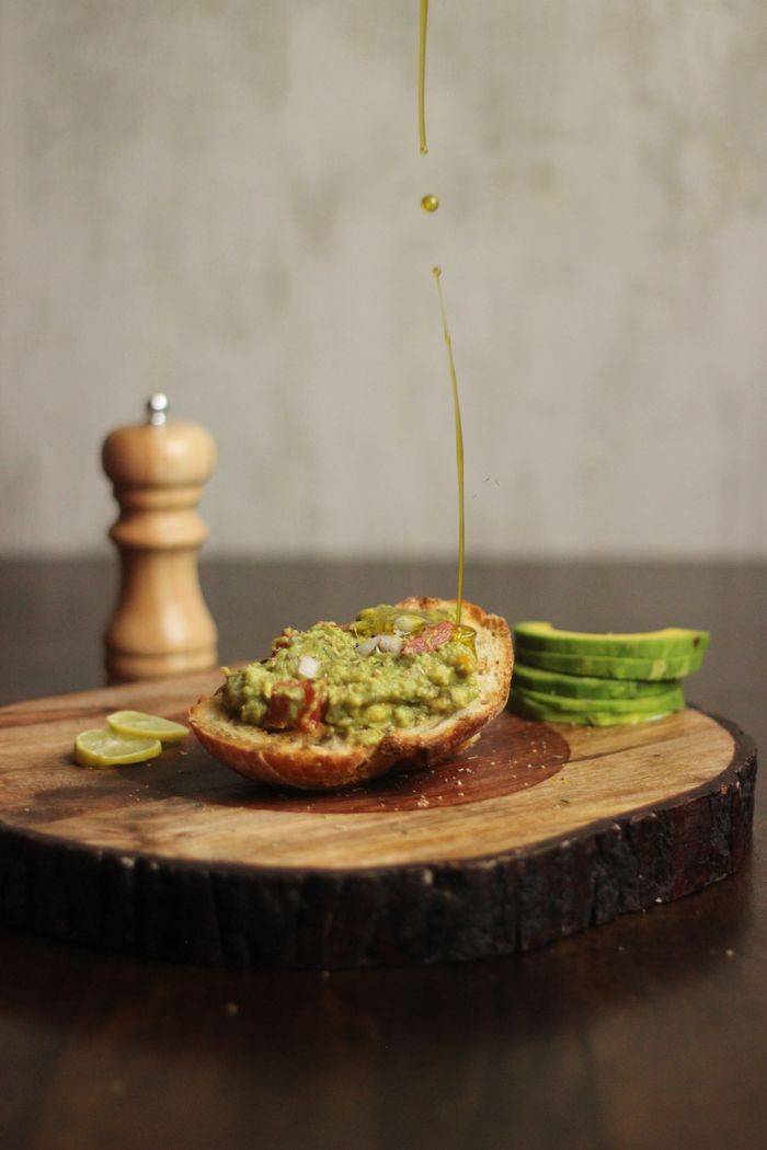 Close-up of an avocado toast with a drizzle of olive oil, on a rustic wooden board.