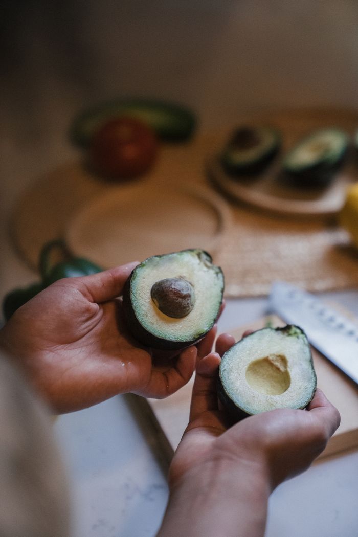 gallery-4 Close-up of hands holding ripe avocado halves in a cozy kitchen ambiance.